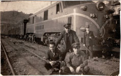 Ramn Botana Garca, a la izquierda, posando en la estacin de Oviedo frente a una composicin remolcada por la locomotora elctrica 7746 de RENFE, junto a otros compaeros, dos a su lado vestidos con uniforme y gorra sin identificar, y otro al fondo con uniforme, gorra y bandern, posiblemente, jefe de estacin o bien factor - Dcada de 1970 - Oviedo