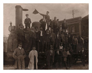 Personal de la estacin de Zaragoza - Arrabal posando en la estacin ante una locomotora de vapor. Entre ellos puede observarse, en primera fila a la izquierda de todo, con un guardapolvo oscuro, las manos en los bolsillos, gorra y pauelo blanco, a Nicols Larroche Rivars, que fue factor en dicha estacin.