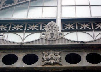 Detalle de la ornamentacin en hierro de la marquesina que, antao, estuvo en el pabelln de llegadas del edificio de viajeros. Esta marquesina fue trasladada a la entrada actual al Museo del Ferrocarril. Detrs, frontn acristalado y celosas de ventilacin de hierro recortado.